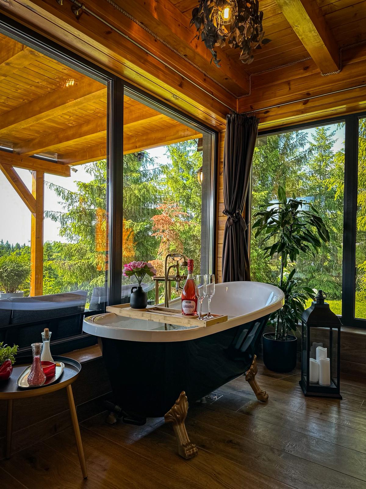 Elegant black clawfoot bathtub in bedroom with forest views and champagne setup