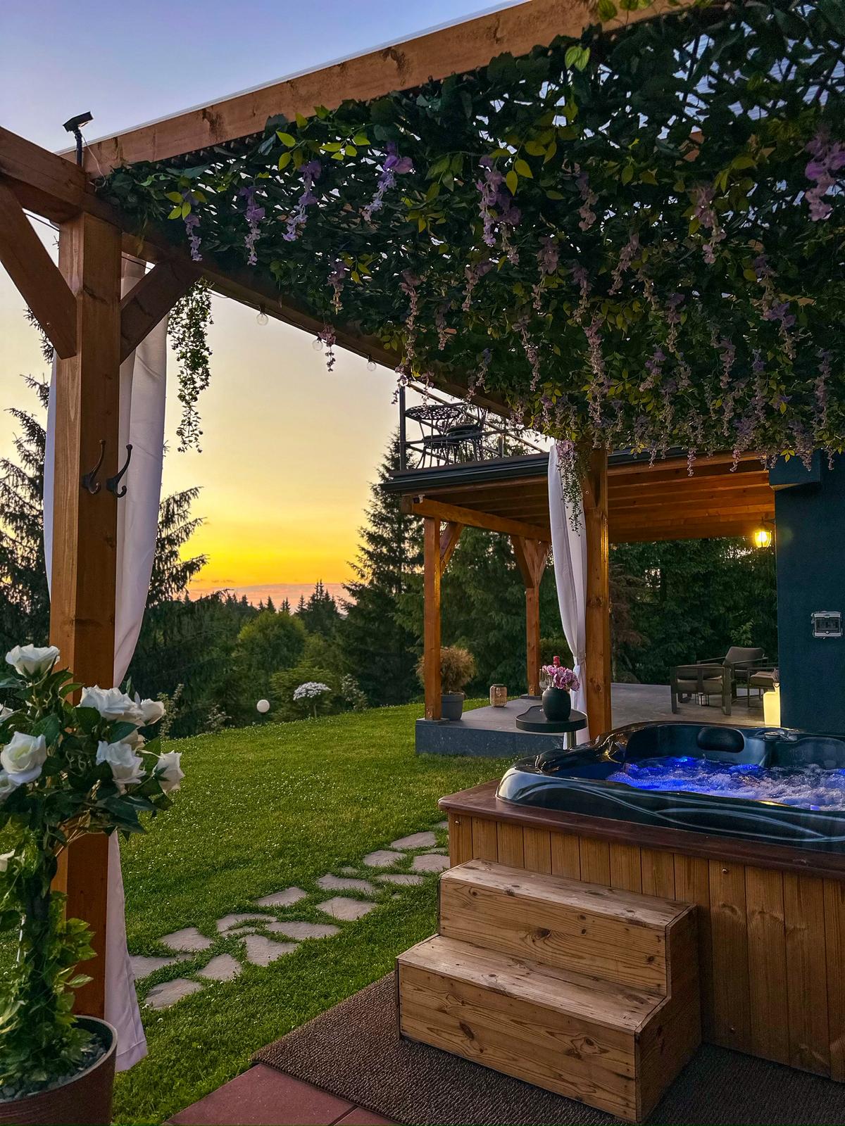 Outdoor jacuzzi with blue LED lights under wisteria pergola at sunset with mountain forest views